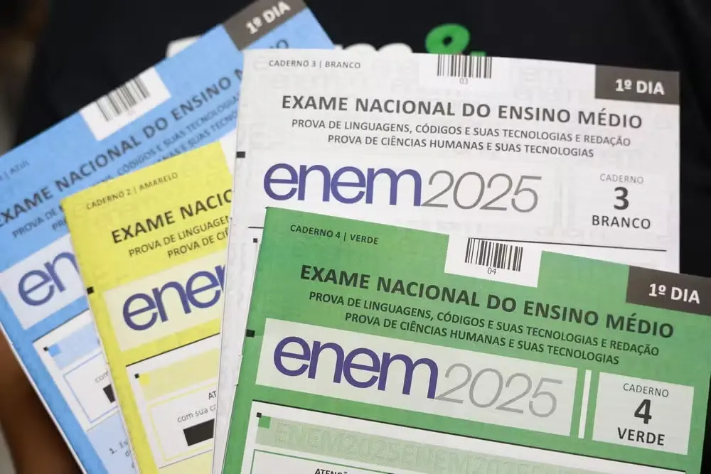 Visão detalhada de múltiplos cadernos de prova coloridos do ENEM 2025, destacando o '1º DIA' e as matérias de Linguagens, Códigos e Redação, e Ciências Humanas.