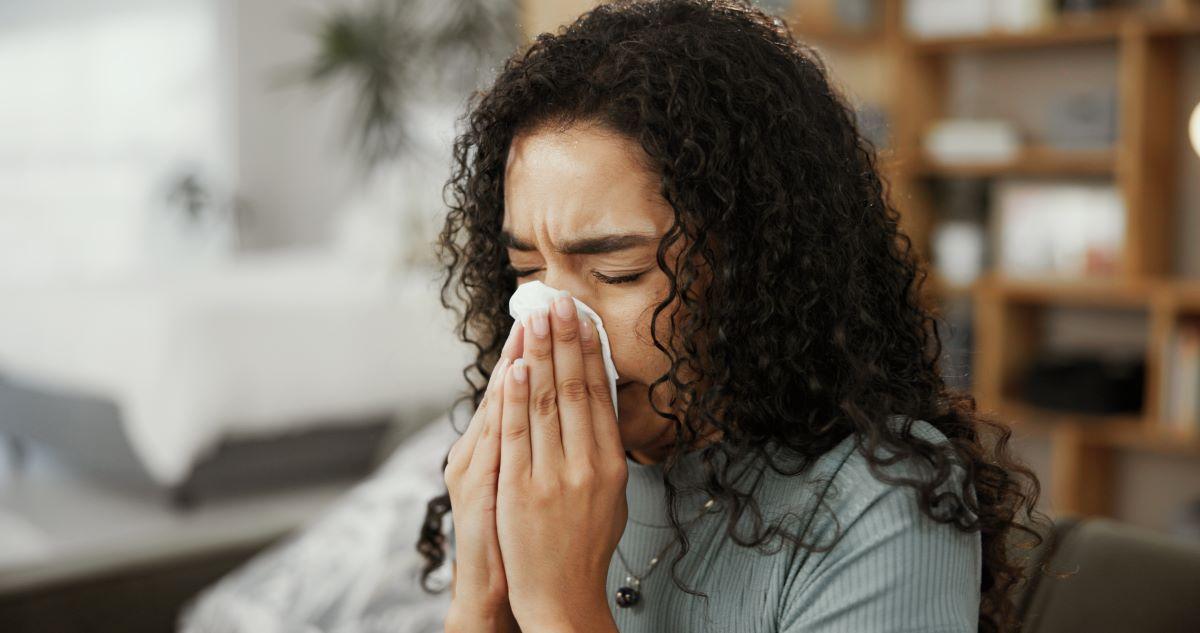 Pessoa de cabelos cacheados em ambiente doméstico, assoando o nariz com um lenço.
