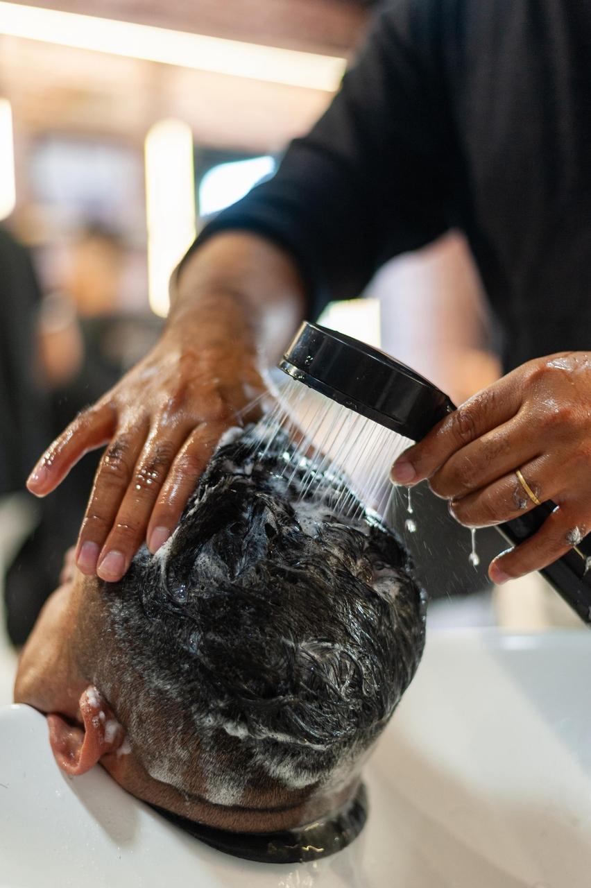 Homem lavando cabelo em cadeira específica para isso, em barbearia.