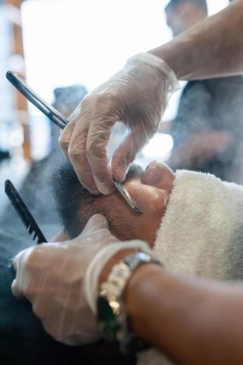 Barbeiro fazendo a barba de um homem com navalha.