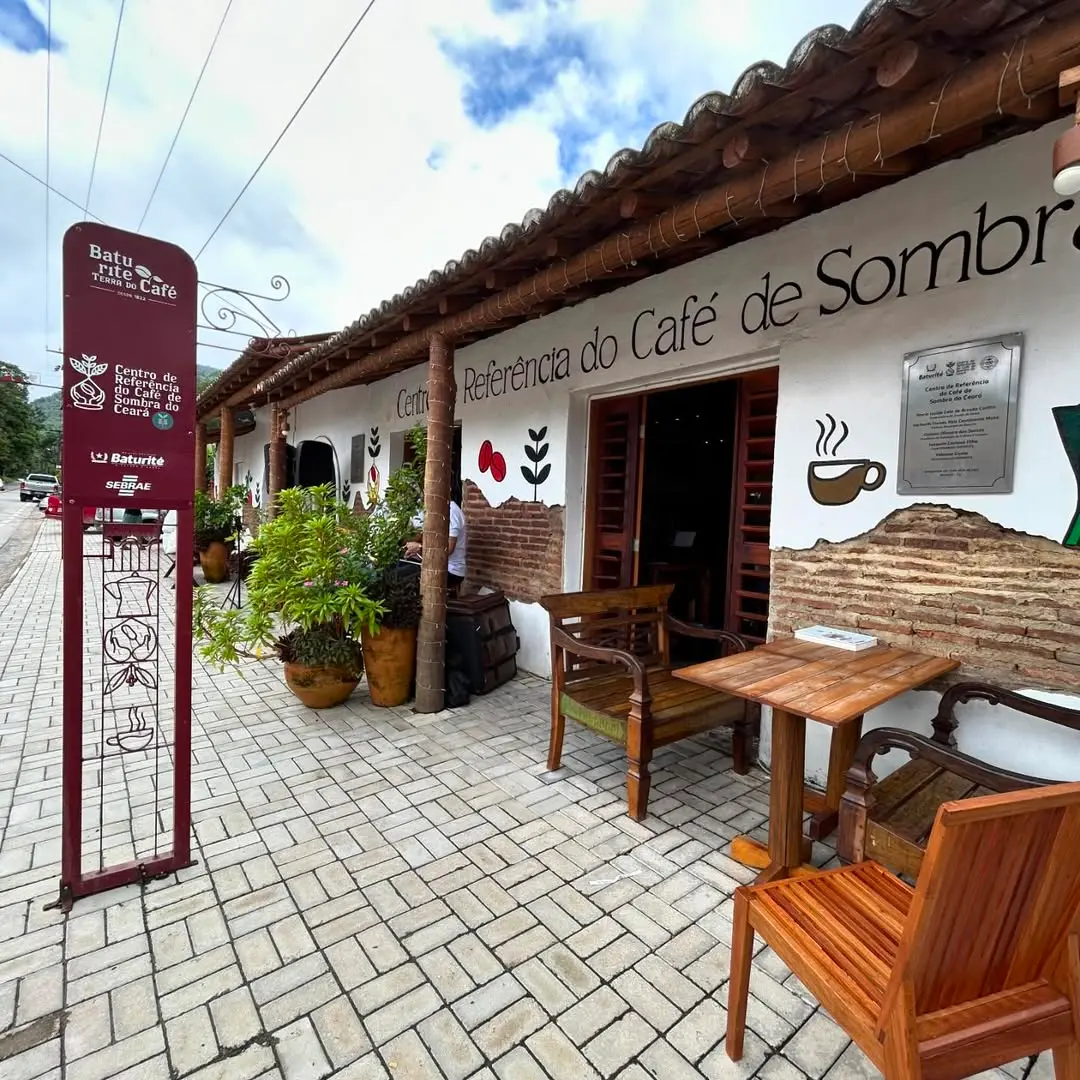 Fachada do Centro de Referência do Café de Sombra, um espaço dedicado ao cultivo sustentável de café sob sombra, com ambientes rústicos e decorativos relacionados ao café, sob céu azul com nuvens.