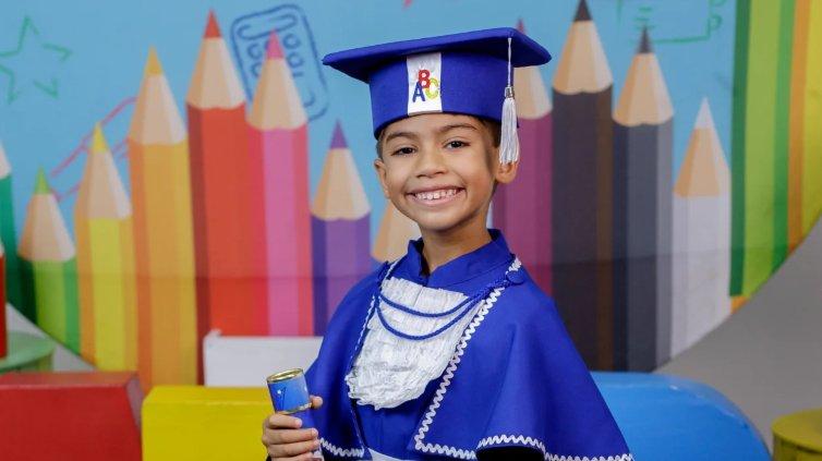 Imagem mostra Benício Xavier sorridente com toga e capelo azuis de formatura, segurando um diploma em um fundo colorido de lápis de cor. Criança faleceu após receber dose de adrenalina errada em Manaus, no Amazonas.