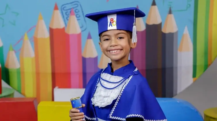 Imagem mostra Benício Xavier sorridente com toga e capelo azuis de formatura, segurando um diploma em um fundo colorido de lápis de cor. Criança faleceu após receber dose de adrenalina errada em Manaus, no Amazonas.