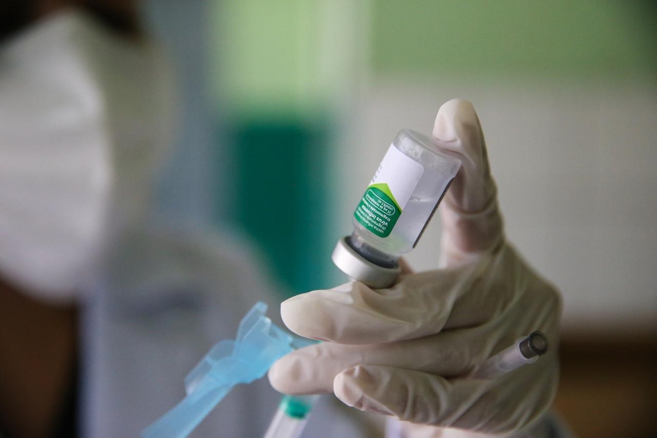 Profissional de saúde preparando uma dose de vacina contra a gripe, com o frasco e a seringa em destaque para aplicação.