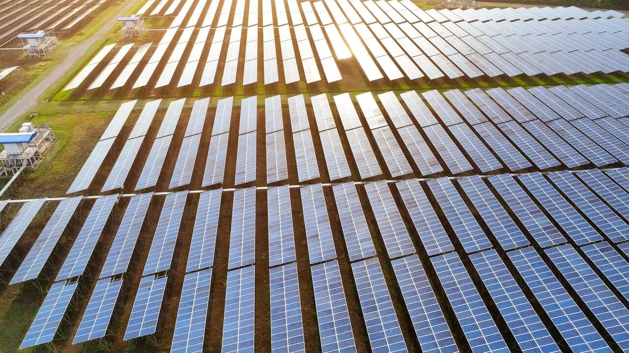 Vista aérea de usina de energia solar, com fileiras de painéis fotovoltaicos instalados em área aberta e refletindo a luz do sol.