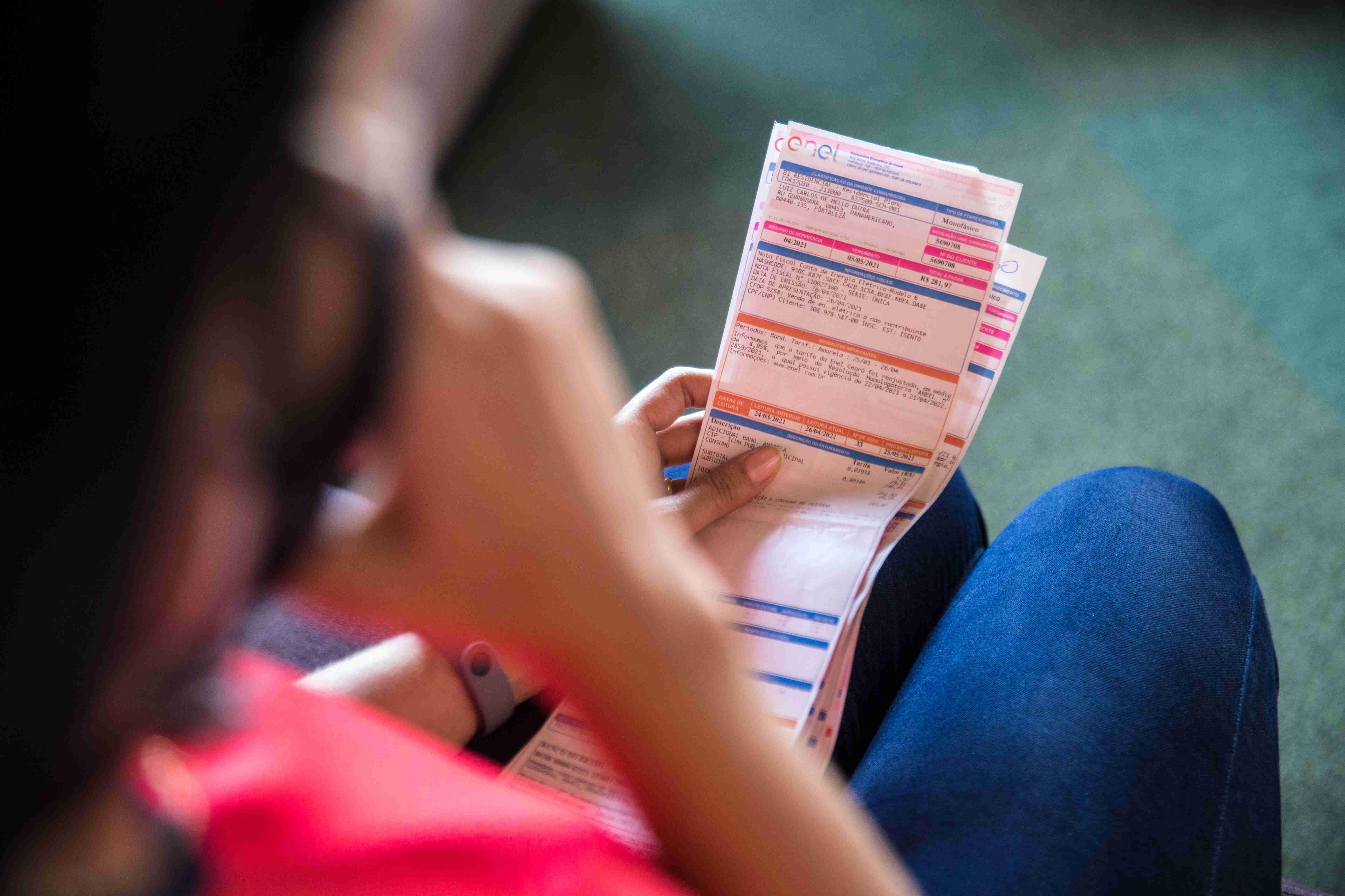Mulher ao telefone e com contas da Enel na mão.