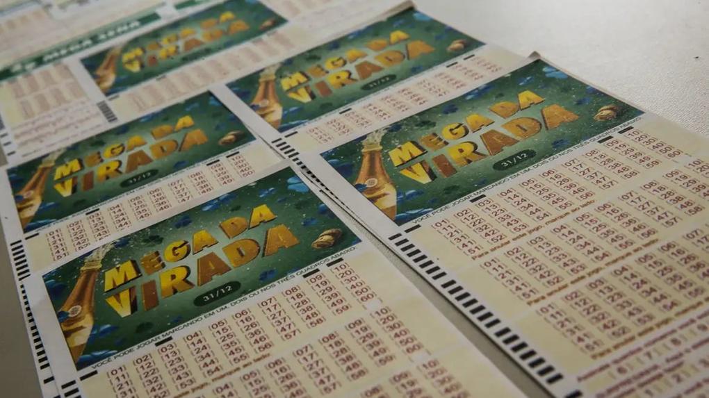 Várias apostas impressas da Mega da Virada estão dispostas sobre uma superfície clara. Cada volante mostra o logotipo “Mega da Virada” com fundo verde, elementos festivos e a data “31/12”, além das tabelas de números para marcação.
