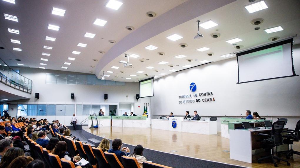 Auditório do Tribunal de Contas do Estado do Ceará durante sessão pública, com conselheiros à mesa principal e plateia sentada acompanhando a apresentação.