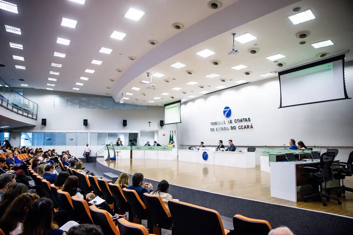 Auditório do Tribunal de Contas do Estado do Ceará durante sessão pública, com conselheiros à mesa principal e plateia sentada acompanhando a apresentação.