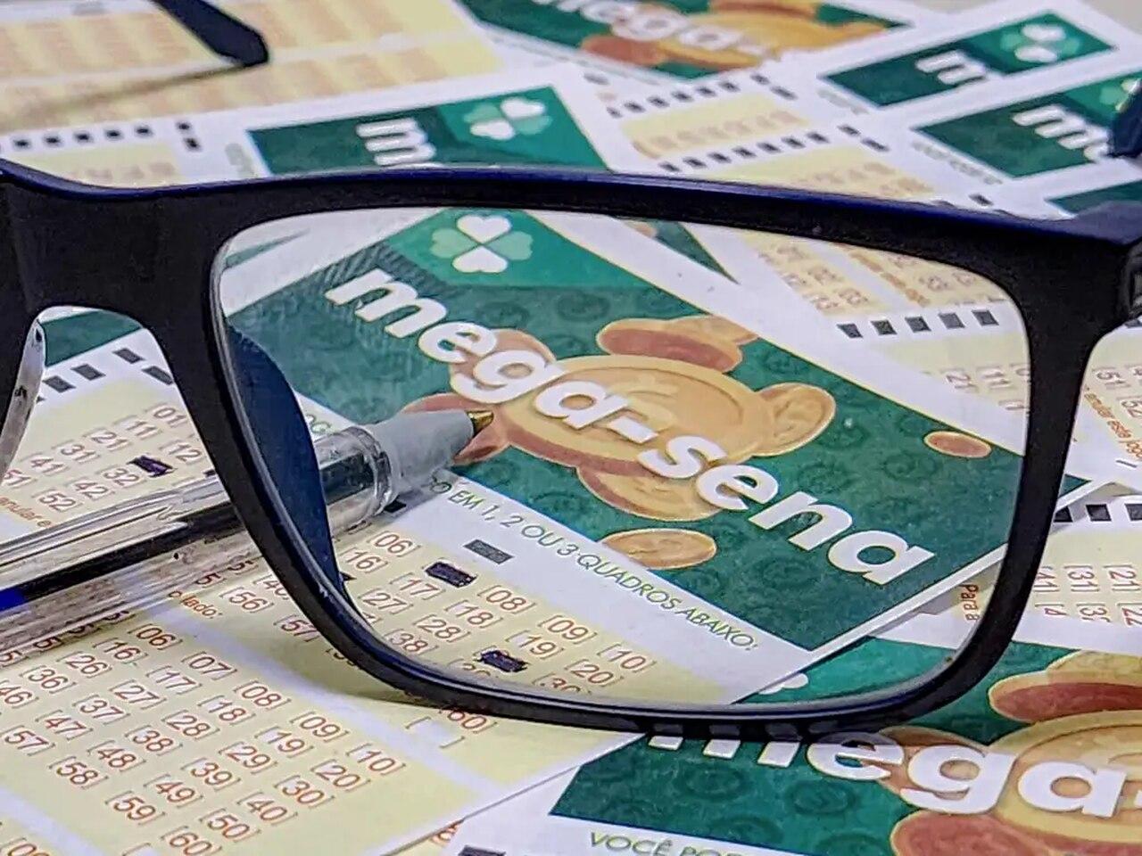 Lente de óculos preto de grau. No fundo, cartelas de aposta com os dizeres 