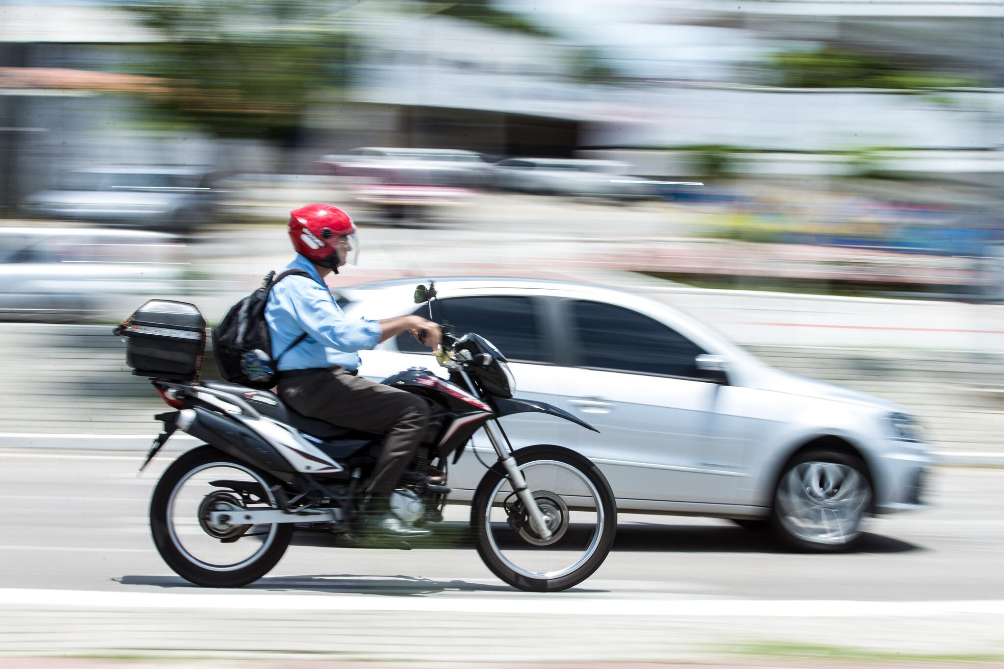 Moto e carro em deslocamento, em foco, com o fundo da imagem desfocado, mostrando movimento.