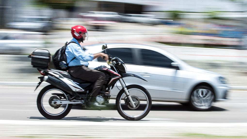 Moto e carro em deslocamento, em foco, com o fundo da imagem desfocado, mostrando movimento.