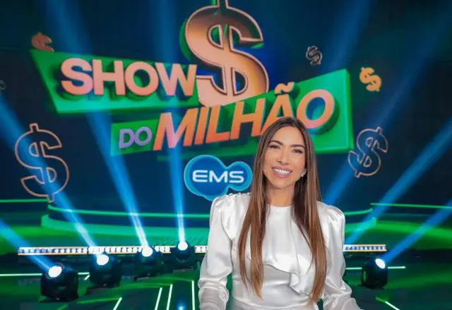 Apresentadora Patrícia Abravanel sorridente em estúdio de programa de televisão, com cenário iluminado ao fundo e o logotipo ‘Show do Milhão’ em destaque.