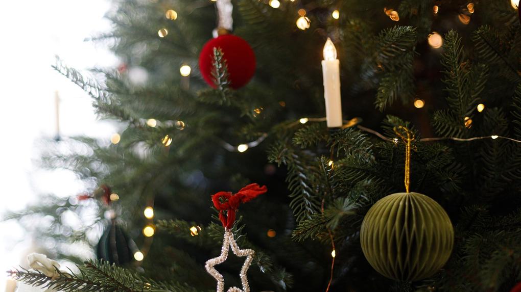 Galhos verdes de árvore de Natal, decorada com bola verde, vela decorativa, estrela prata e bola vermelha, além de luzes douradas.