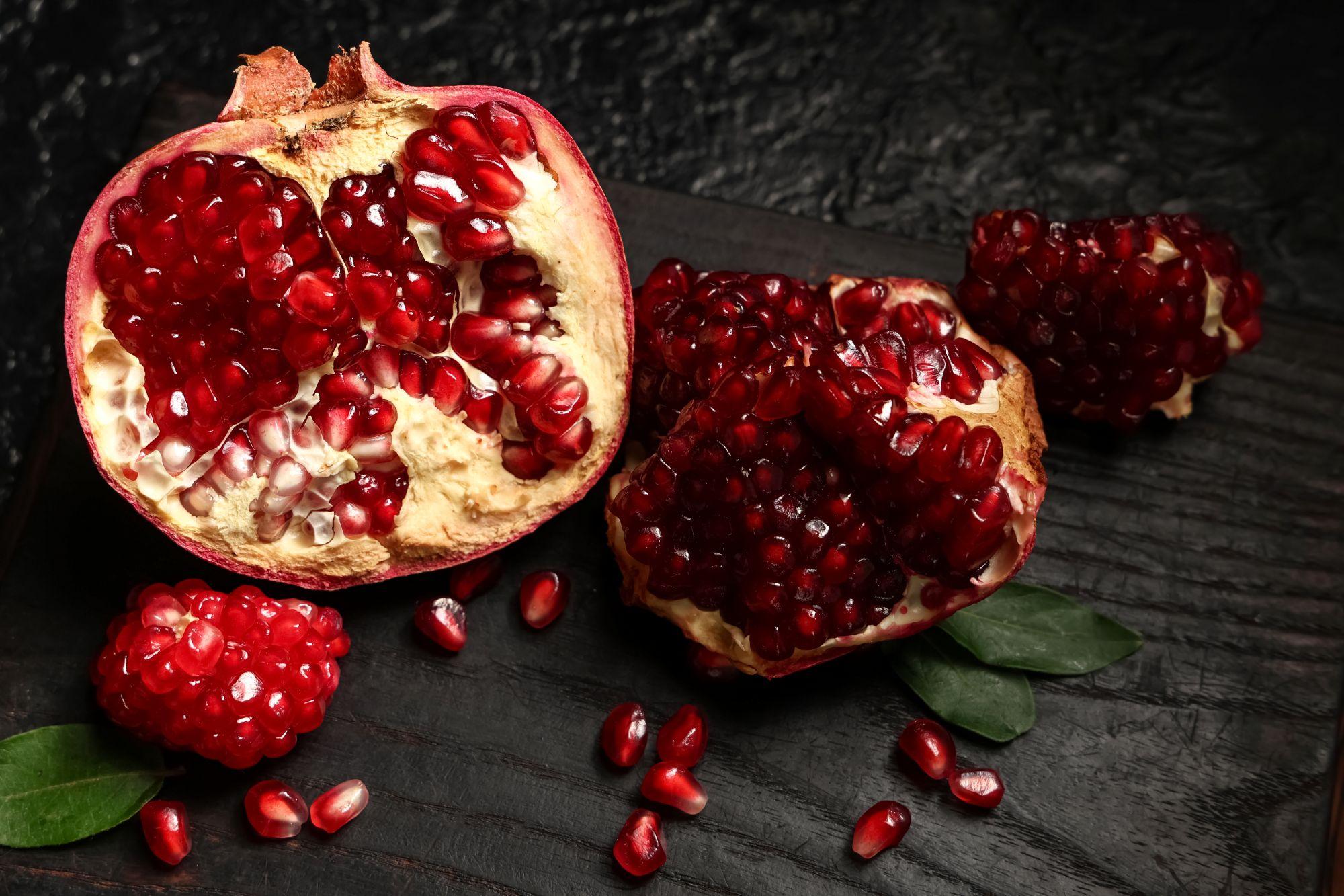 Placa de madeira com romã fresca cortada e sementes sobre fundo preto, closeup
