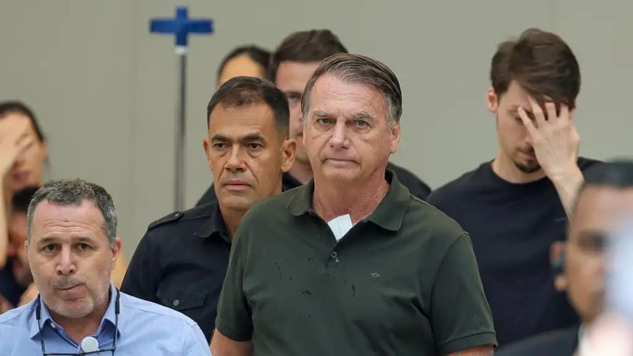 Ex-presidente Jair Bolsonaro em aparição pública, com um curativo no pescoço, cercado por sua equipe.