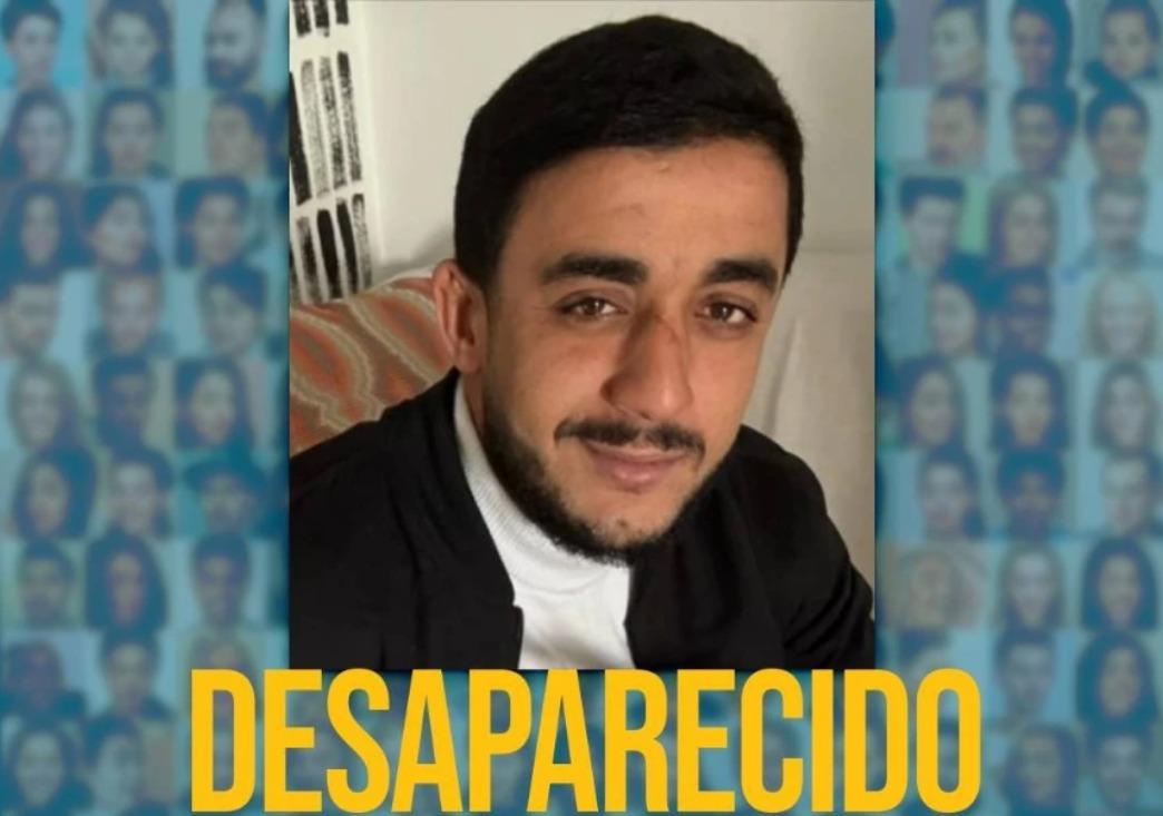 A imagem mostra um homem pardo, com barba e cabelo preto, vestido com uma roupa preta e branca. Em volta, há a imagem de vários rostos e o nome Desaparecido.