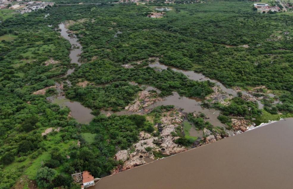 Vista aérea de uma paisagem natural verdejante com um grande rio ou reservatório de água barrenta e áreas de mata ciliar alagadas entre afloramentos rochosos.