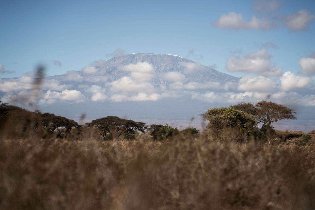 Imagem de longe do monte Kilimanjaro, no Quênia, mostrando vegetação e nuvens no céu.