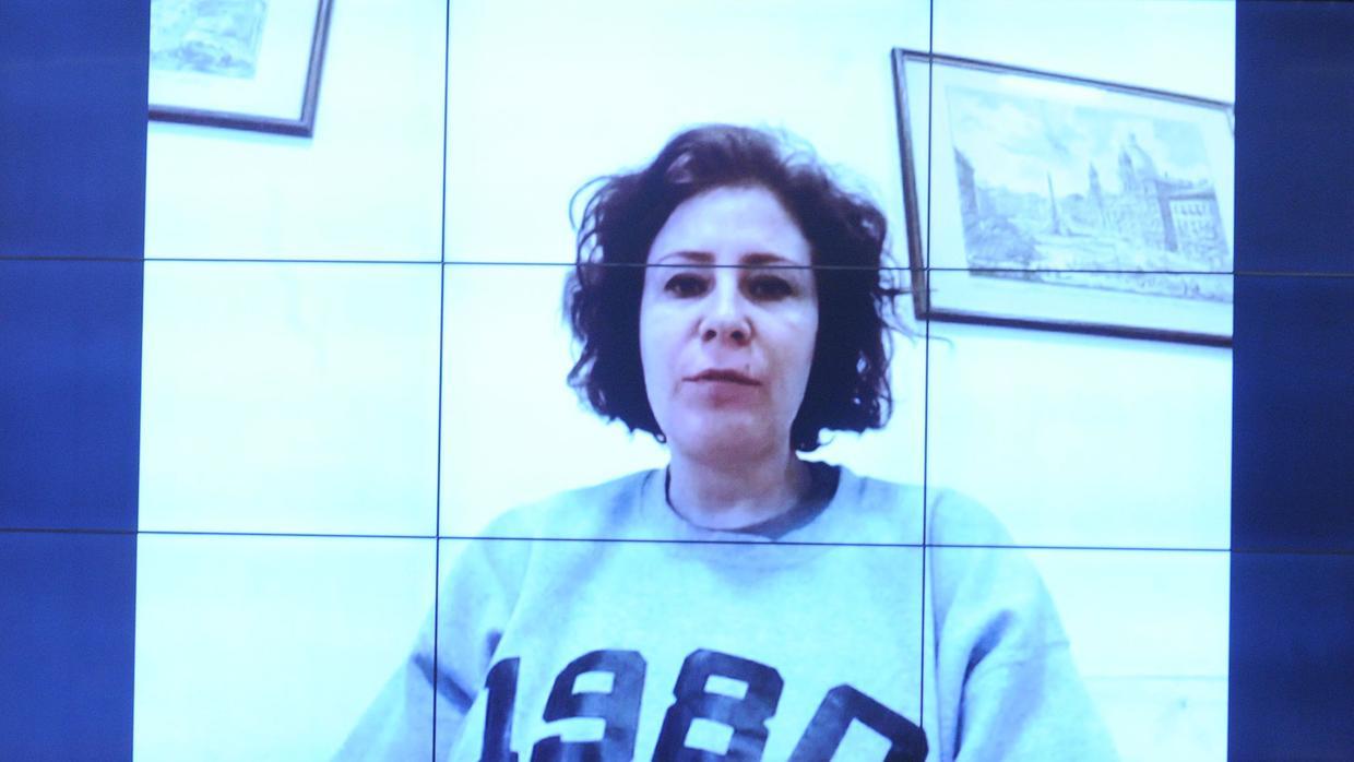 A imagem mostra uma mulher branca, cabelo médio de cor escura, vestida com um moletom claro, com o número 1980, em uma videoconferência.