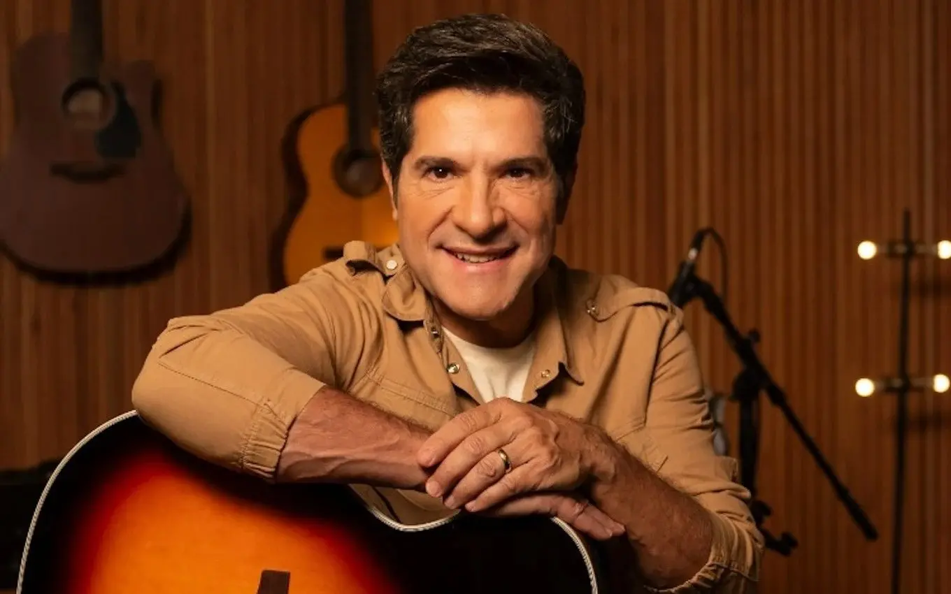 Imagem mostra o cantor Daniel sorridente, segurando um violão em um ambiente de estúdio, promovendo o programa Viver Sertanejo, da TV Globo, do qual é apresentador.