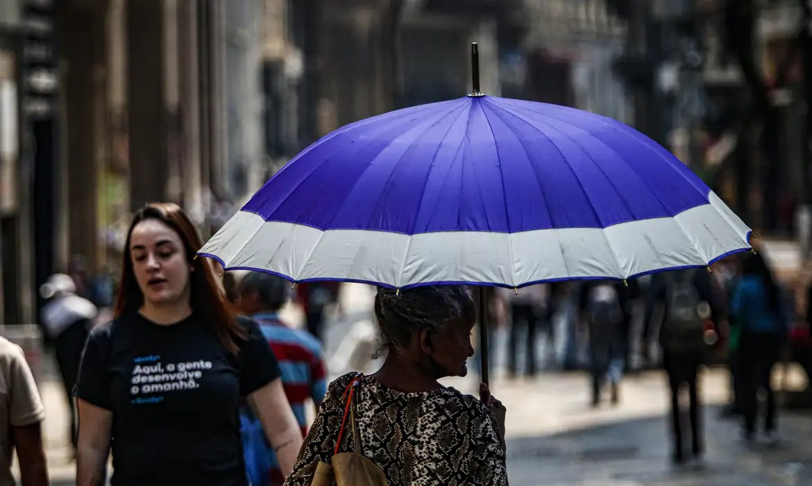 Foto que contém mulher segurando guarda-chuva em meio a onda de calor em cidade brasileira.