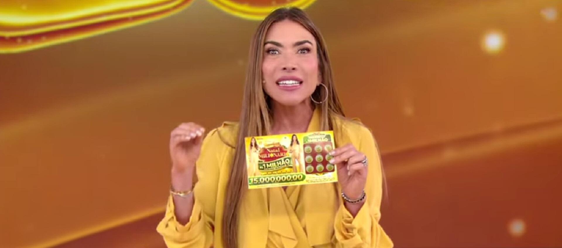 Patrícia Abravanel segurando uma tele sena no palco do programa onde é realizado o sorteio.