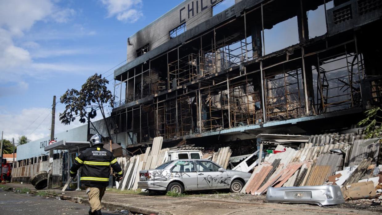 A imagem mostra um bombeiro saindo da frente da Sucata Chico Alves que foi incendiada, em Fortaleza.