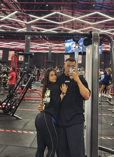 Imagem mostra o casal Caique Teixeira Borri, e Flávia Acassia da Silva, em ambiente interno de uma academia de ginástica.