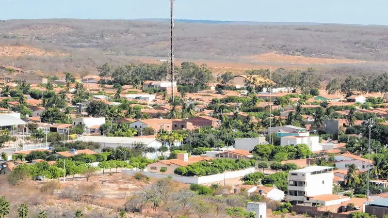 Vista aérea de Croatá, com casas de telhados de barro, muitas árvores verdes, uma torre de comunicação e colinas secas no horizonte sob céu claro.