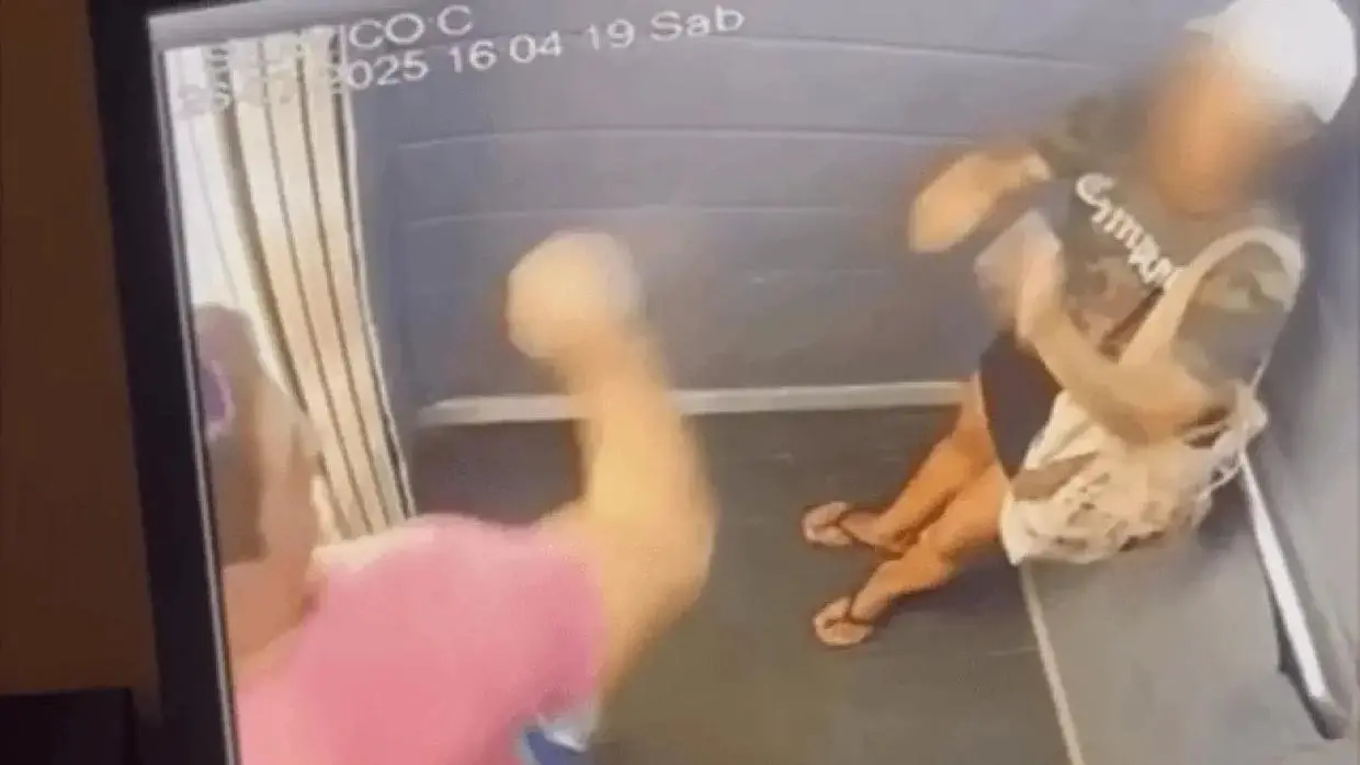 Na imagem, homem com braço em punho ameaça mulher dentro de elevador.