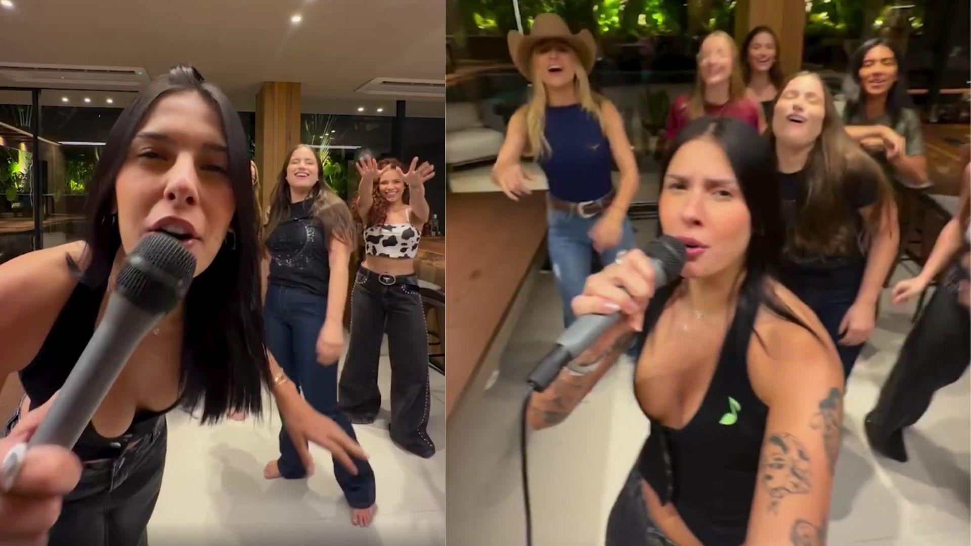A cantora Ana Castela, de cabelos pretos e lisos, segura microfone próximo à boca, com amigas ao fundo da imagem.