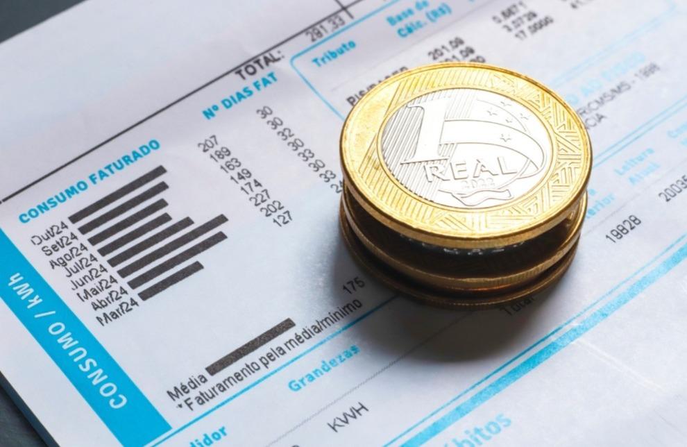 Conta de energia com moedas de 1 real em cima.
