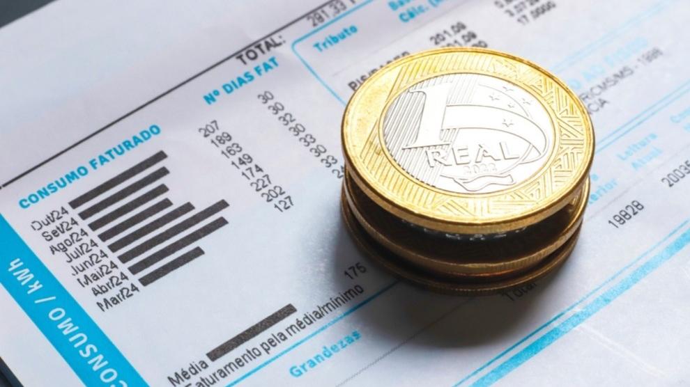 Conta de energia com moedas de 1 real em cima.