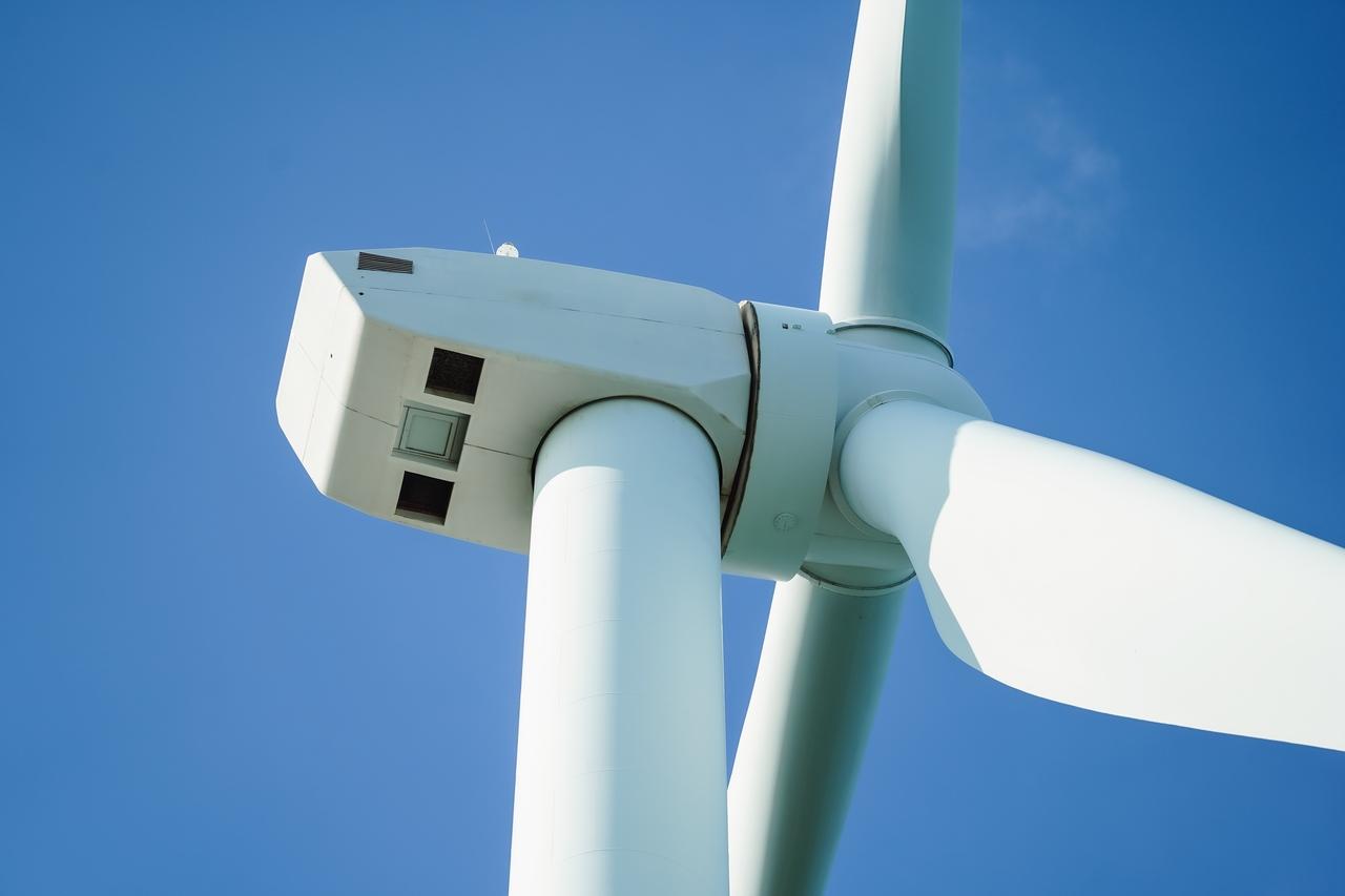 Detalhe de aerogerador com pás e nacelle de turbina eólica em destaque contra céu azul, representando geração de energia renovável.