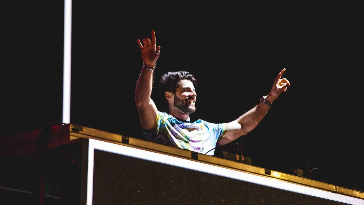 Alok com braços levantados, atrás de pick up de som.