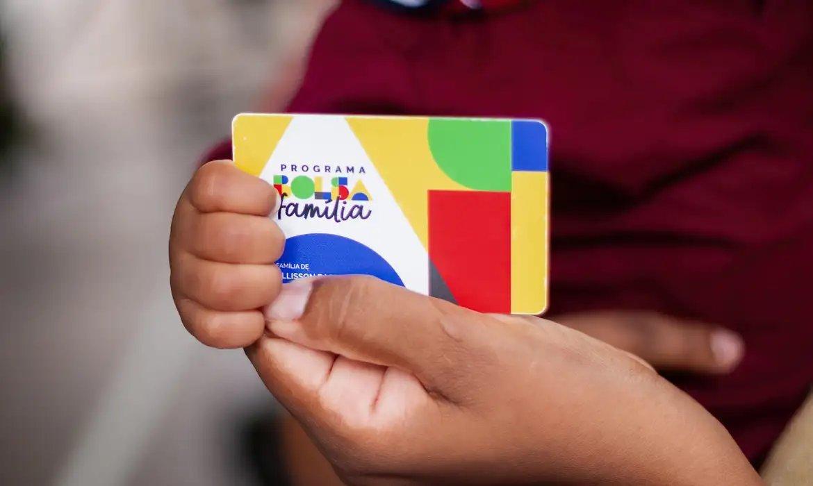 Foto que contém pessoa segurando o cartão do Bolsa Família.