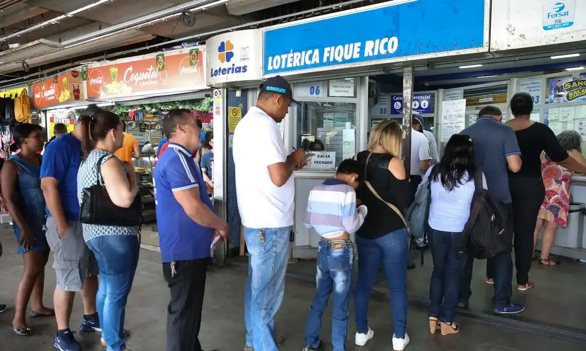 Pessoas dentro de uma fila para entrar numa casa lotérica.