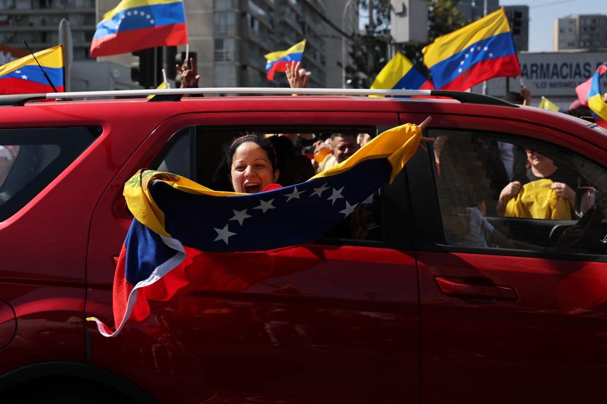 Venezuelana dentro de carro nas ruas do Chile com bandeira da Venezuela comemorando captura de Nicolás Maduro pelos EUA.