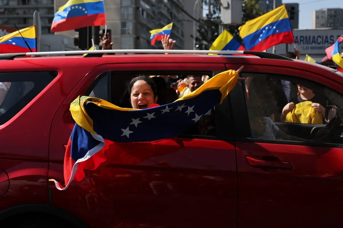 Venezuelana dentro de carro nas ruas do Chile com bandeira da Venezuela comemorando captura de Nicolás Maduro pelos EUA.