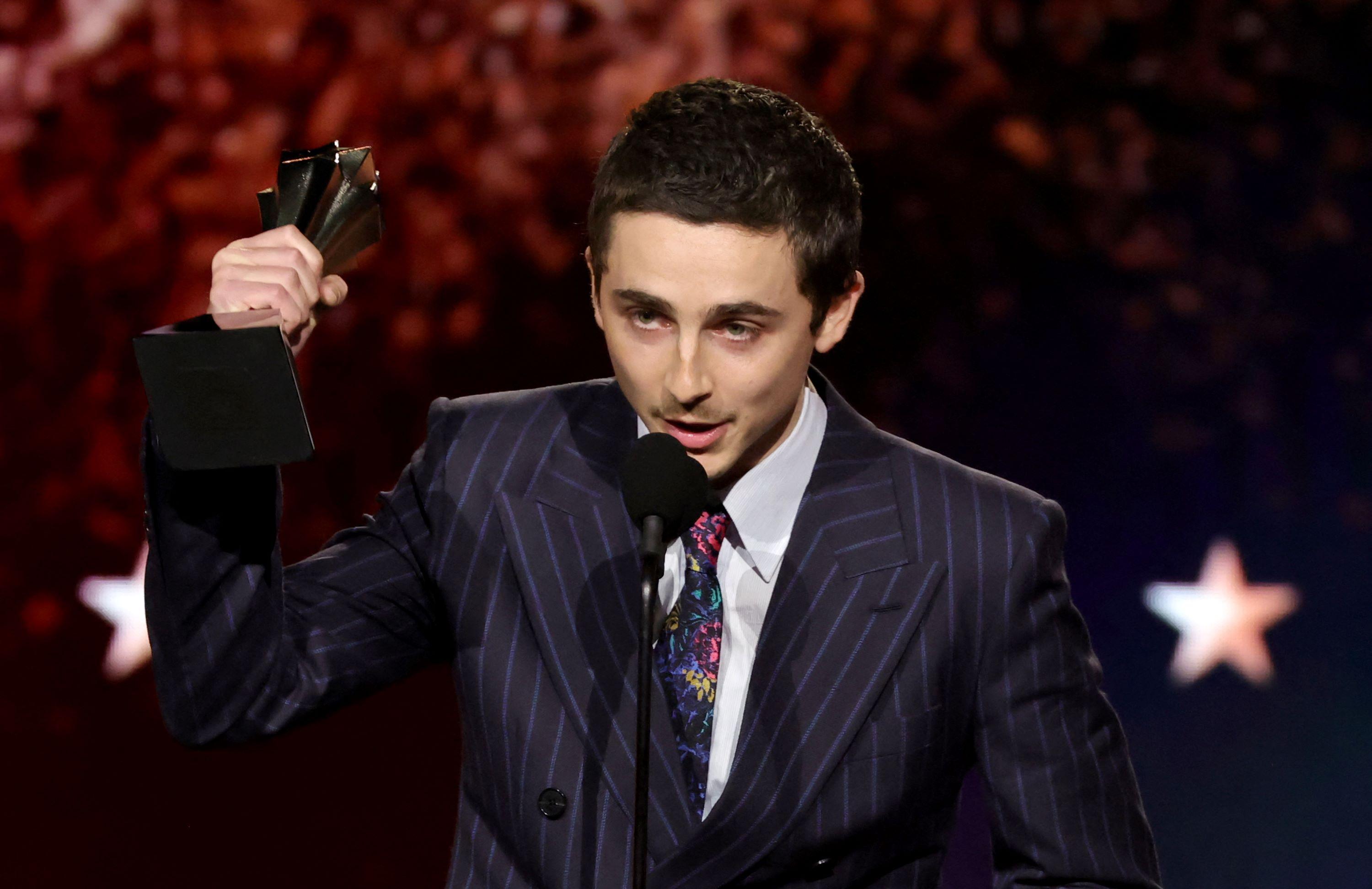ator Timothée Chalamet levantando o troféu do prêmio de melhor ator por Marty Supreme, no Critics Choice Awards. ele fala ao microfone.