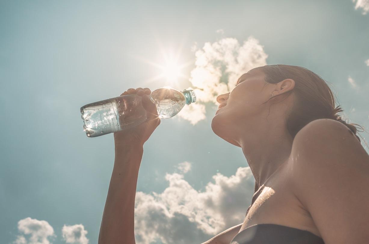 Mulher bebendo água ilustra matéria sobre baixa umidade do ar.