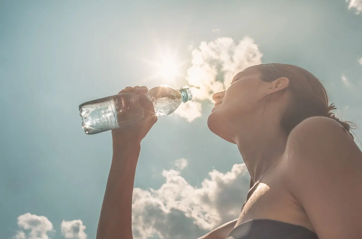 Mulher bebendo água ilustra matéria sobre baixa umidade do ar.