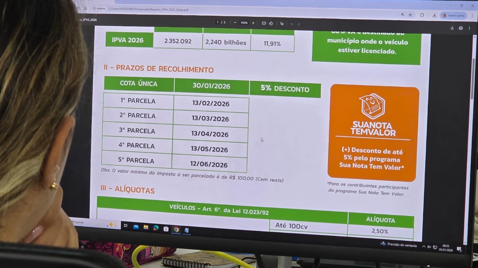 Pessoa sentada em frente a um computador visualizando um documento sobre o IPVA 2026. Na tela, aparece uma tabela com prazos de recolhimento do imposto no Ceará: cota única até 30/01/2026 com 5% de desconto e parcelas mensais de fevereiro a junho de 2026. Ao lado, há um destaque para o programa “Sua Nota Tem Valor”, que oferece desconto adicional de até 5%.
