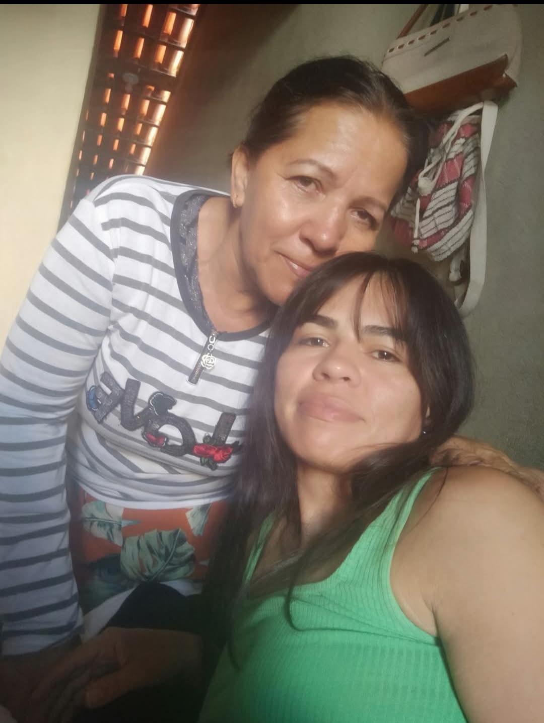 Imagem de duas mulheres venezuelanas sorridentes em um ambiente interno, uma de cabelo curto e a outra de cabelo comprido, com uma atmosfera acolhedora.