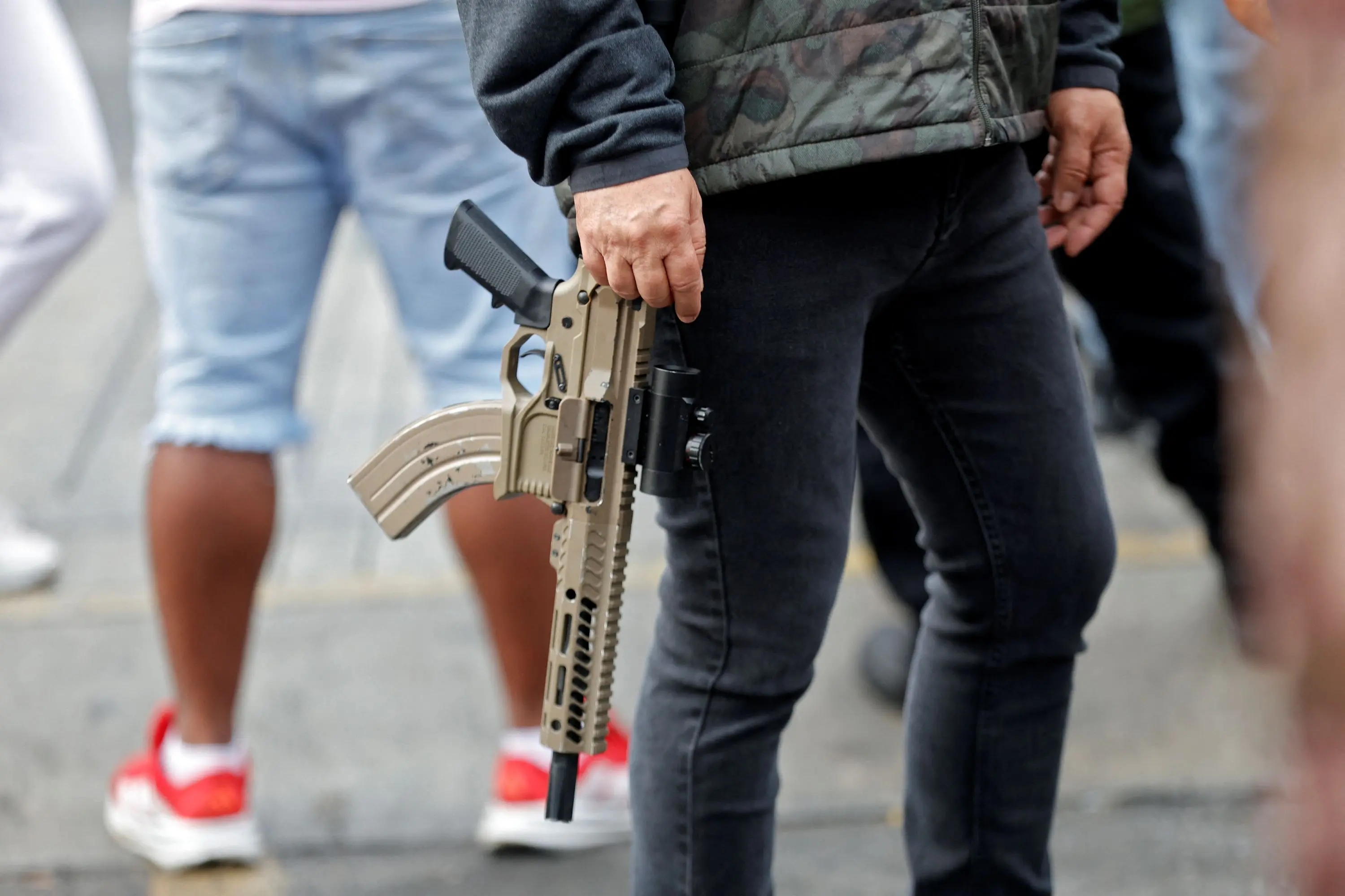 Close-up de um rifle de estilo militar de cor clara sendo segurado firmemente por uma pessoa, destacando a textura e os detalhes da arma. Polícia da Venezuela.