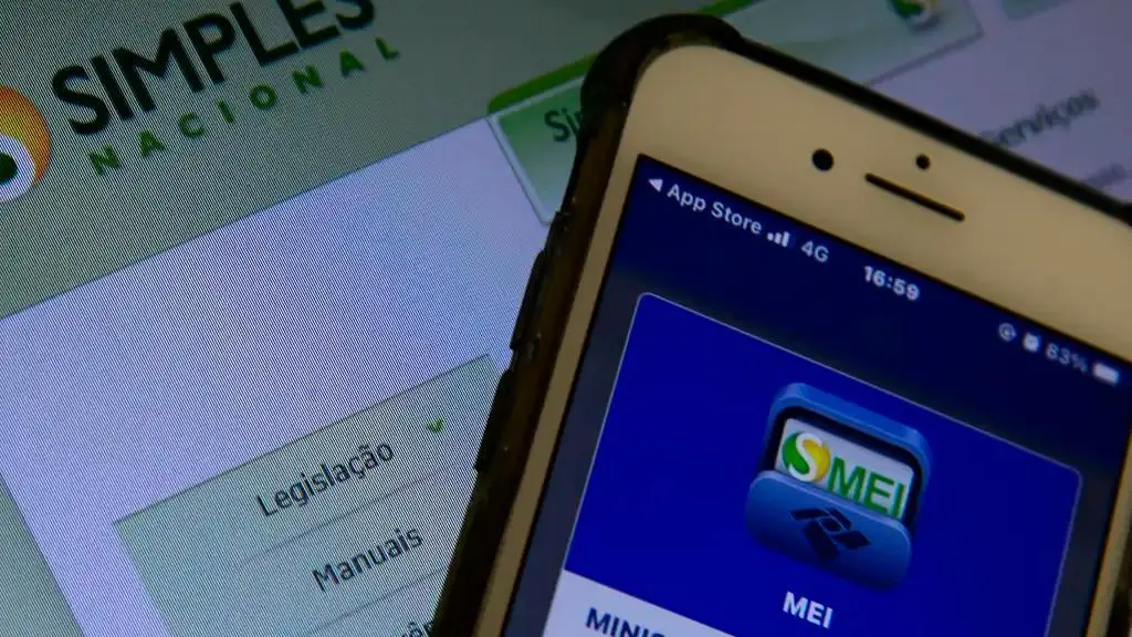 Foto de tela de celular e tela de computador mostrando o site do MEI Simples Nacional da Receita Federal para matéria sobre declaração anual.