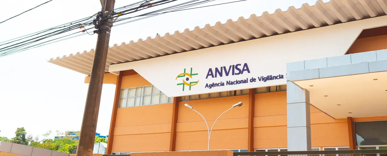 Fachada de prédio laranja com parte de cima branca e logo oficial da Anvisa, seguidos dos dizeres 