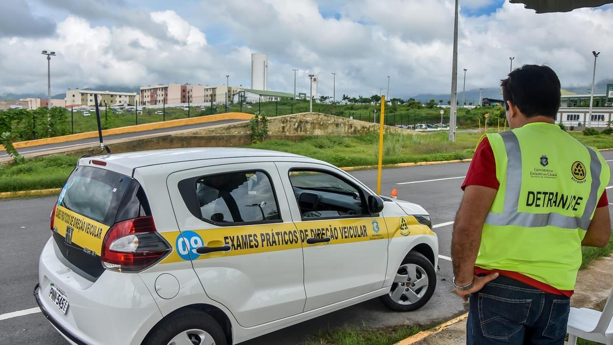 Imagem mostra instrutor do DETRAN Ceará supervisiona um carro de exame prático de direção em uma pista de testes ao ar livre.