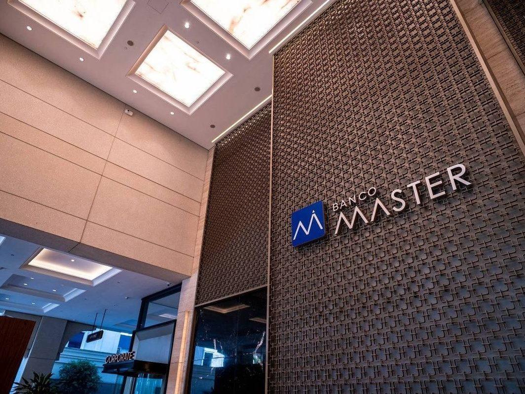 Fachada interna do Banco Master, mostrando o logotipo azul e o nome da instituição em relevo.
